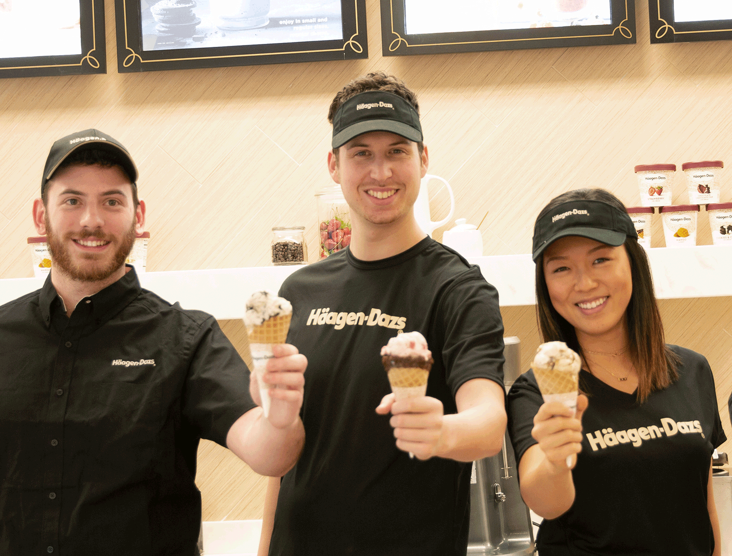 Three Haagen Dazs employees holding out ice cream cones